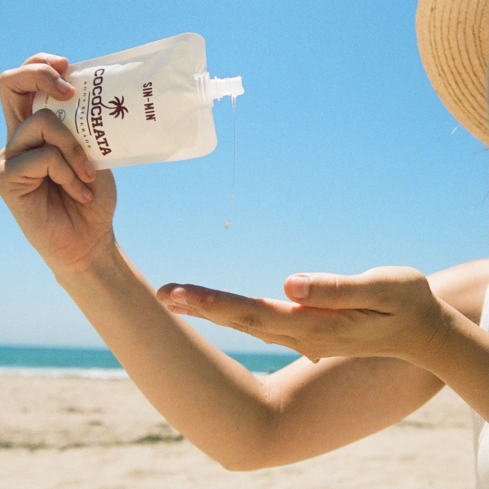 Cocochata Body Beverage being poured from one hand to another with the ocean in the background.