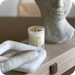 Horchata Candle with a decorative container on a surface next to a marble sculpture