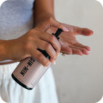 Person holding a pink spray bottle labeled 'SIN-MIN' with a blurred background
