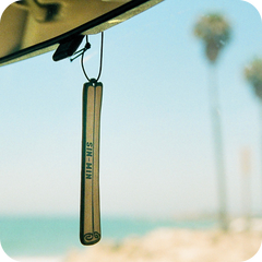 Car air freshener hanging from a car's rearview mirror with a blurred beach background