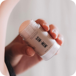 Hand holding a jar of SIN-MIN deodorant against a neutral background