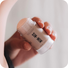 Hand holding a jar of SIN-MIN deodorant against a neutral background