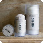 Two sizes of SIN-MIN natural deodorant products on a wooden surface with a neutral background