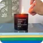 Candle labeled 'Cinnamon Spice and Everything Nice' being lit on a stack of books.
