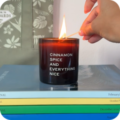 Candle labeled 'Cinnamon Spice and Everything Nice' being lit on a stack of books.