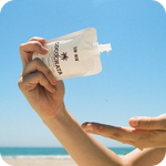 Hand applying Cocochata Body Beverage to another hand with a clear blue sky and beach in the background