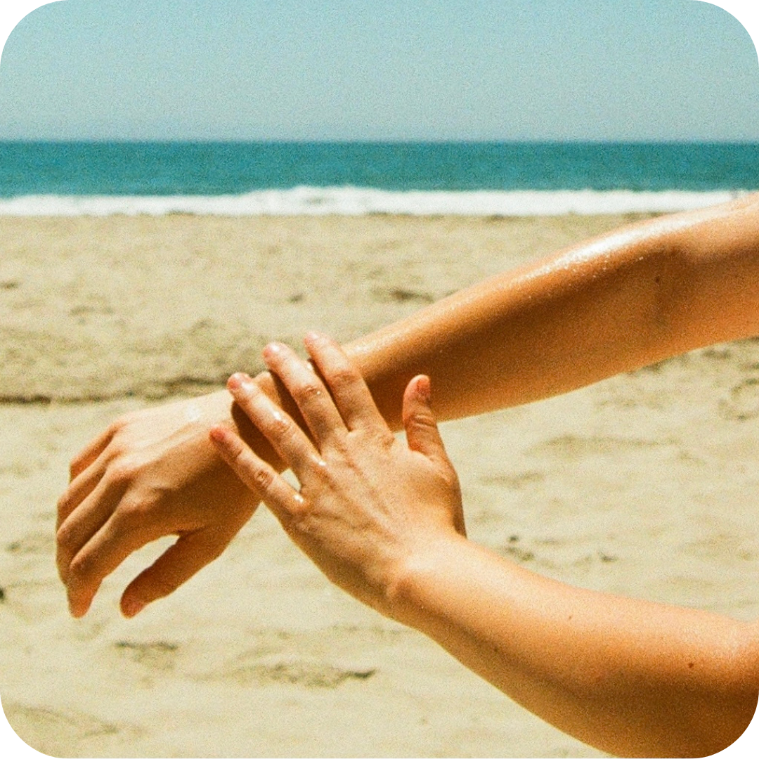 One hand applying Cocochata Body Beverage to an arm on the beach
