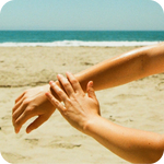 One hand applying Cocochata Body Beverage to an arm on the beach