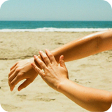 One hand applying Cocochata Body Beverage to an arm on the beach