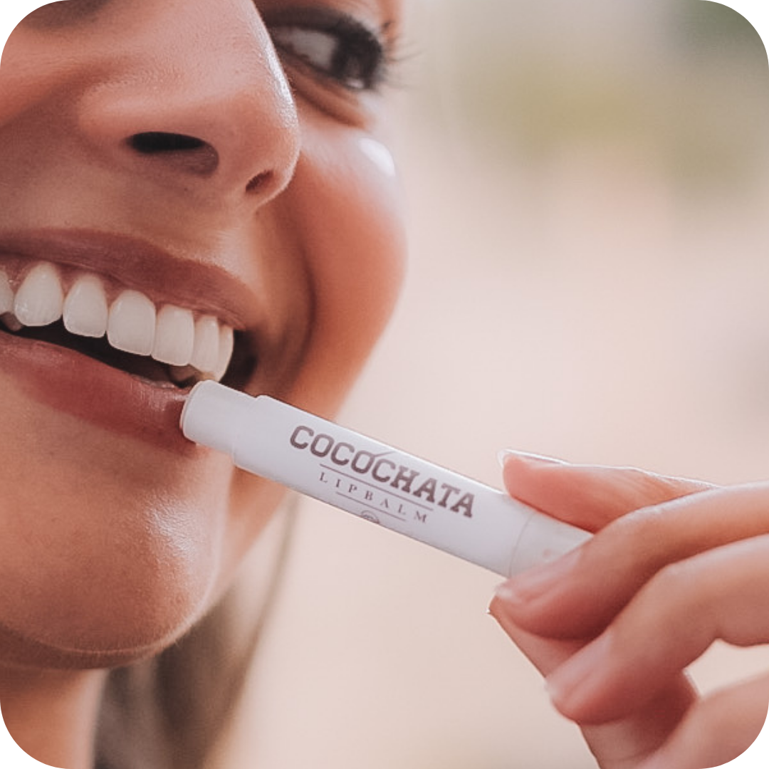 Person applying COCOCHATA lip balm to their lips with a blurred background