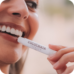 Person applying COCOCHATA lip balm to their lips with a blurred background