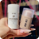 Hand holding two deodorant sticks, one labeled 'Cocochata' and the other 'Sin Min', against a blurred background.