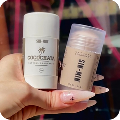 Hand holding two deodorant sticks, one labeled 'Cocochata' and the other 'Sin Min', against a blurred background.