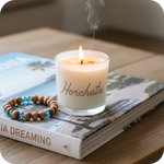 Candle labeled 'Horchata' on a book with a wooden beaded bracelet.