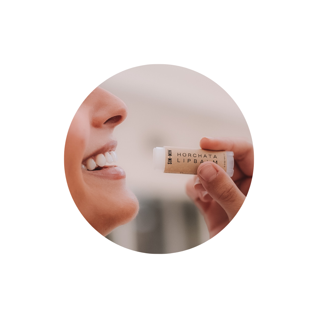 Person applying horchata lip balm to their lips with a blurred background