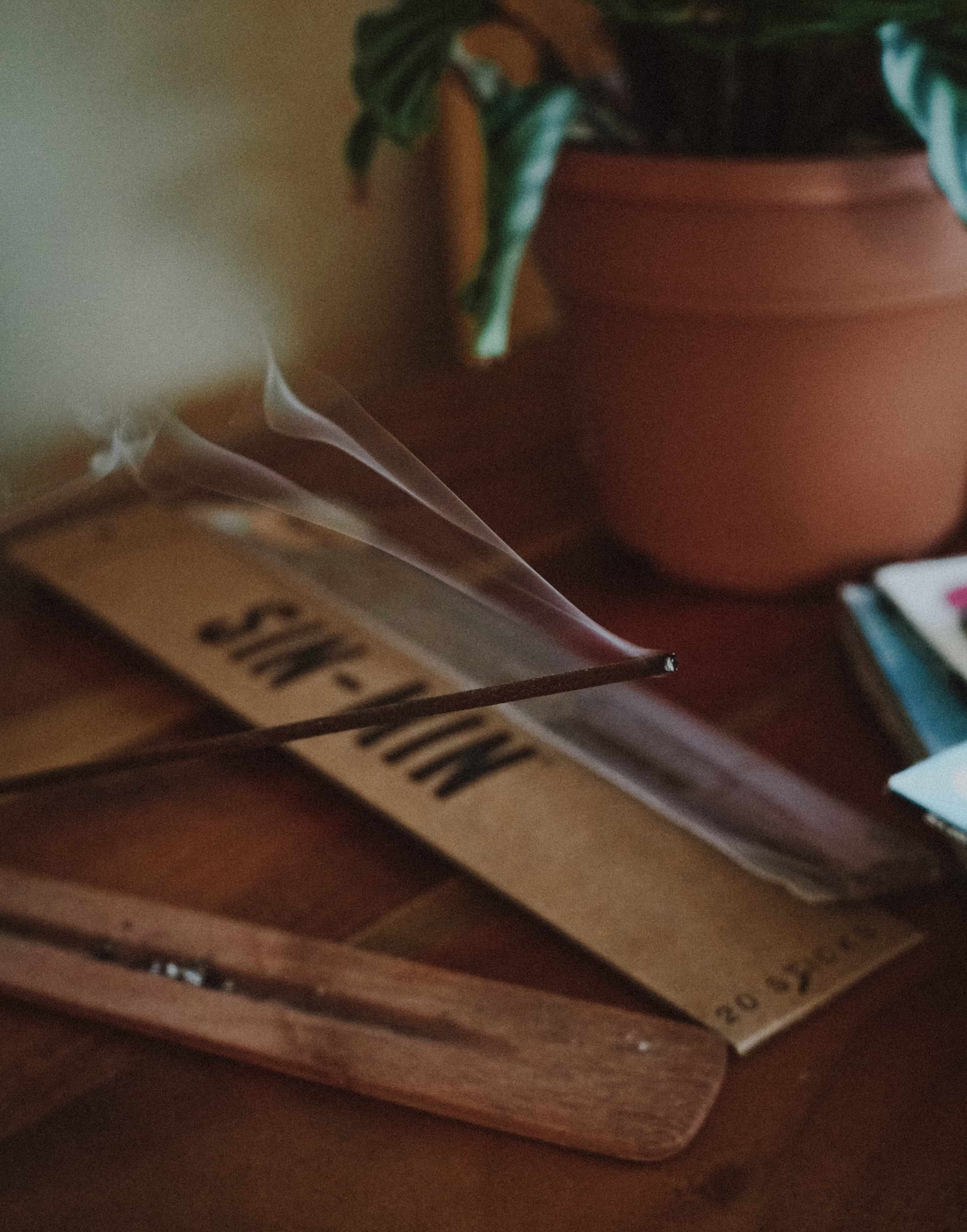 Close up picture of Cincense incense burning on a table with the product packaging and plant in the background