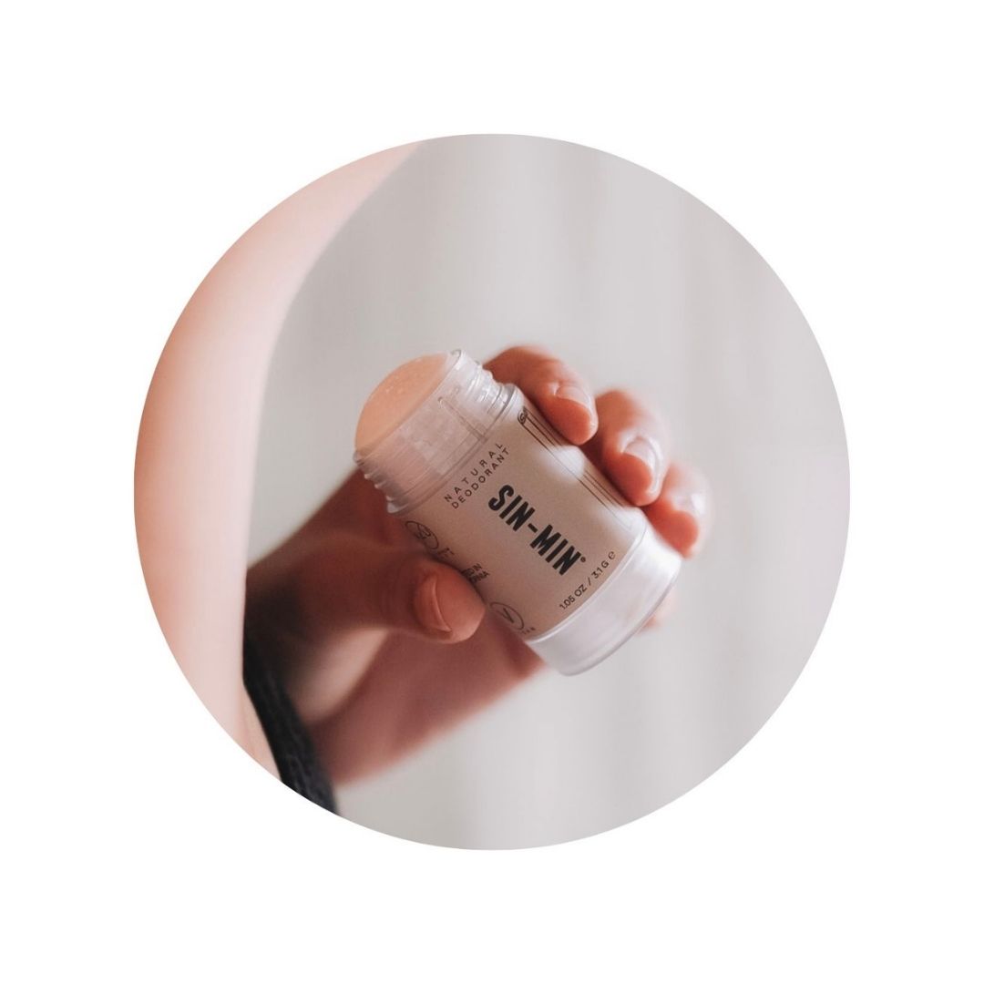 Close up picture of a hand holding SIN-MIN natural deodorant.