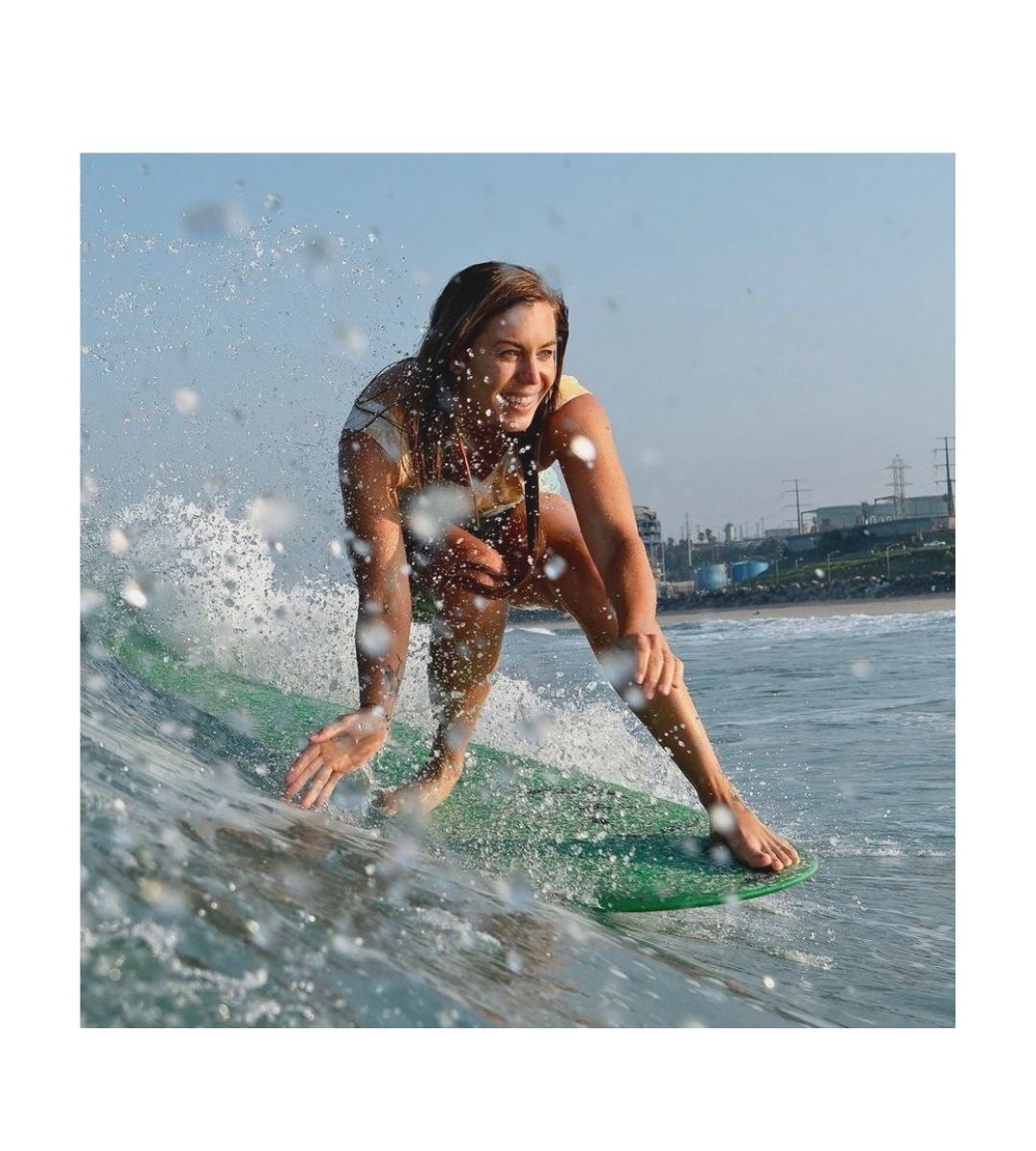 Woman doing a surfing maneuver called a noseride wearing SIN-MIN Shade at El Porto in Los Angeles on a green singlefin longboard