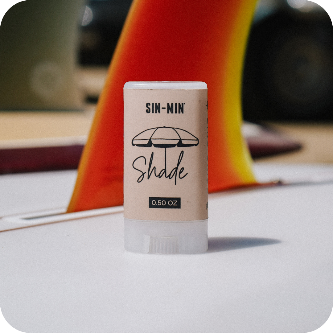 SIN-MIN Shade sunscreen stick with a blurred background of a surfboard fin
