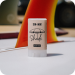SIN-MIN Shade sunscreen stick with a blurred background of a surfboard fin