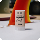 SIN-MIN Shade sunscreen stick with a blurred background of a surfboard fin